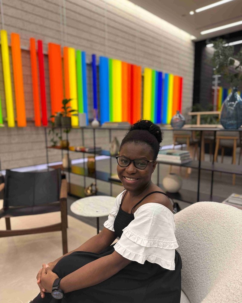 Martha Teiko Teye smiling in front of a colourful rainbow wall installation